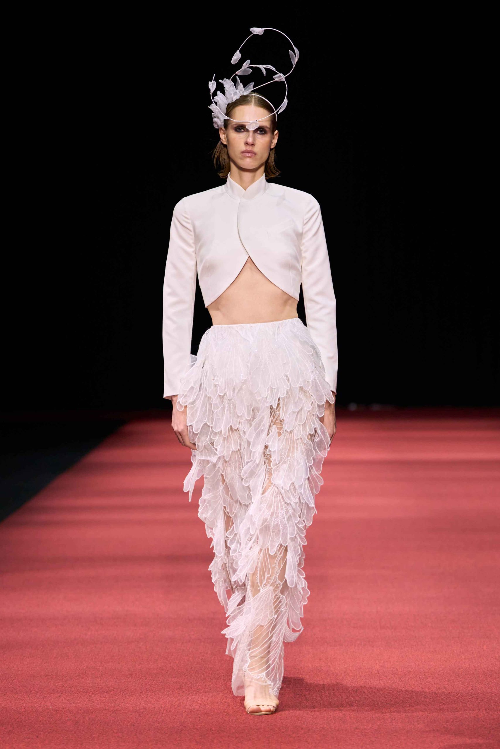Model in a pale pink cropped top and feathered skirt with a sculptural headpiece at the KEL' SS27 show