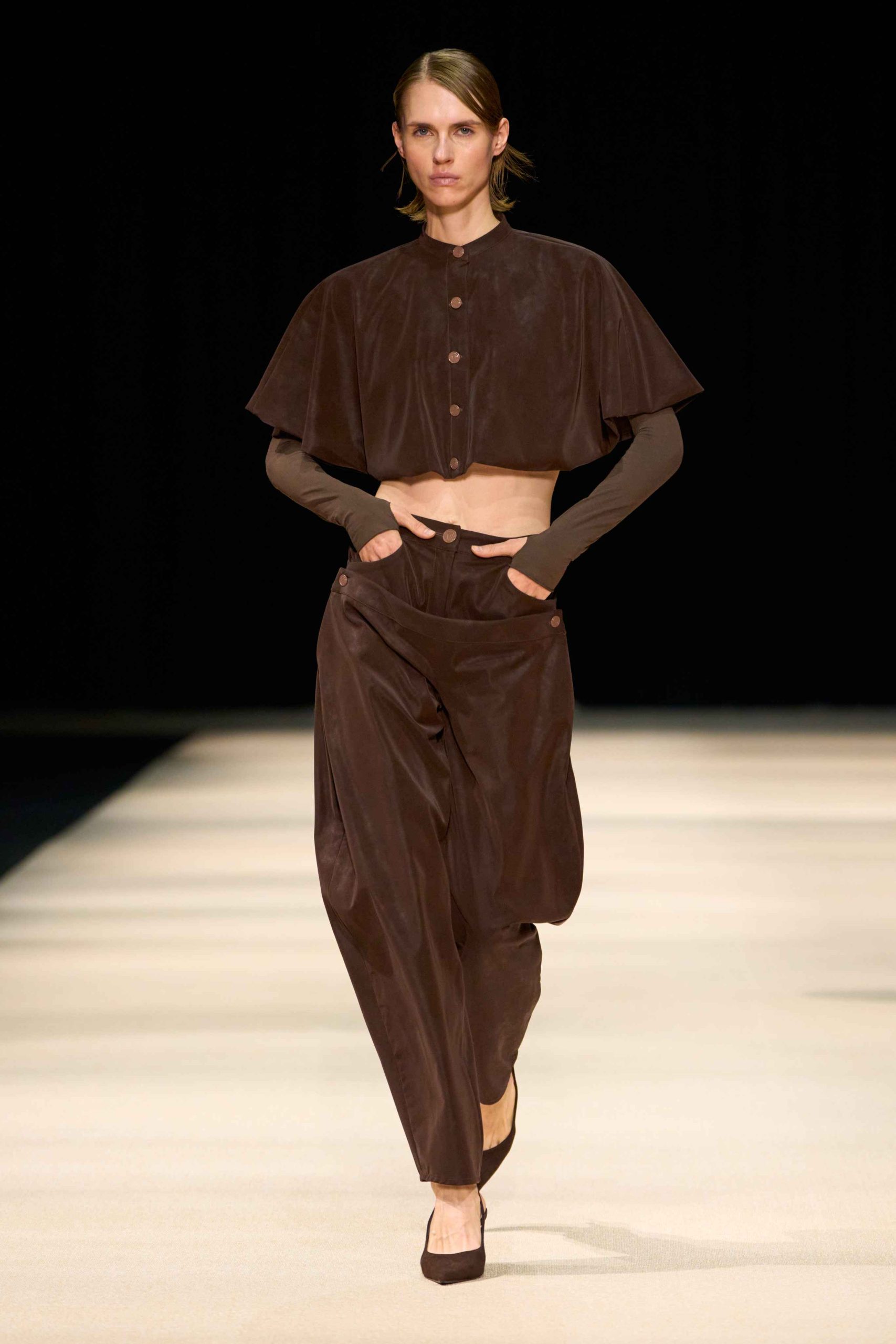 Model in a brown cape-sleeved top and wide trousers at the ODA Store SS27 show